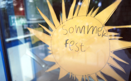An einer Glastour klebt eine selbst gebastelte Sonne - auf diese hat ein Kind "Sommerfest" geschrieben.