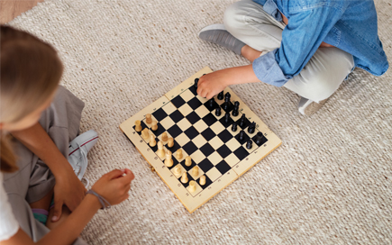 Auf dem Boden sitzend spielen zwei Kinder Schach gegeneinander. Es sich nur die Hände der Kinder zu sehen.